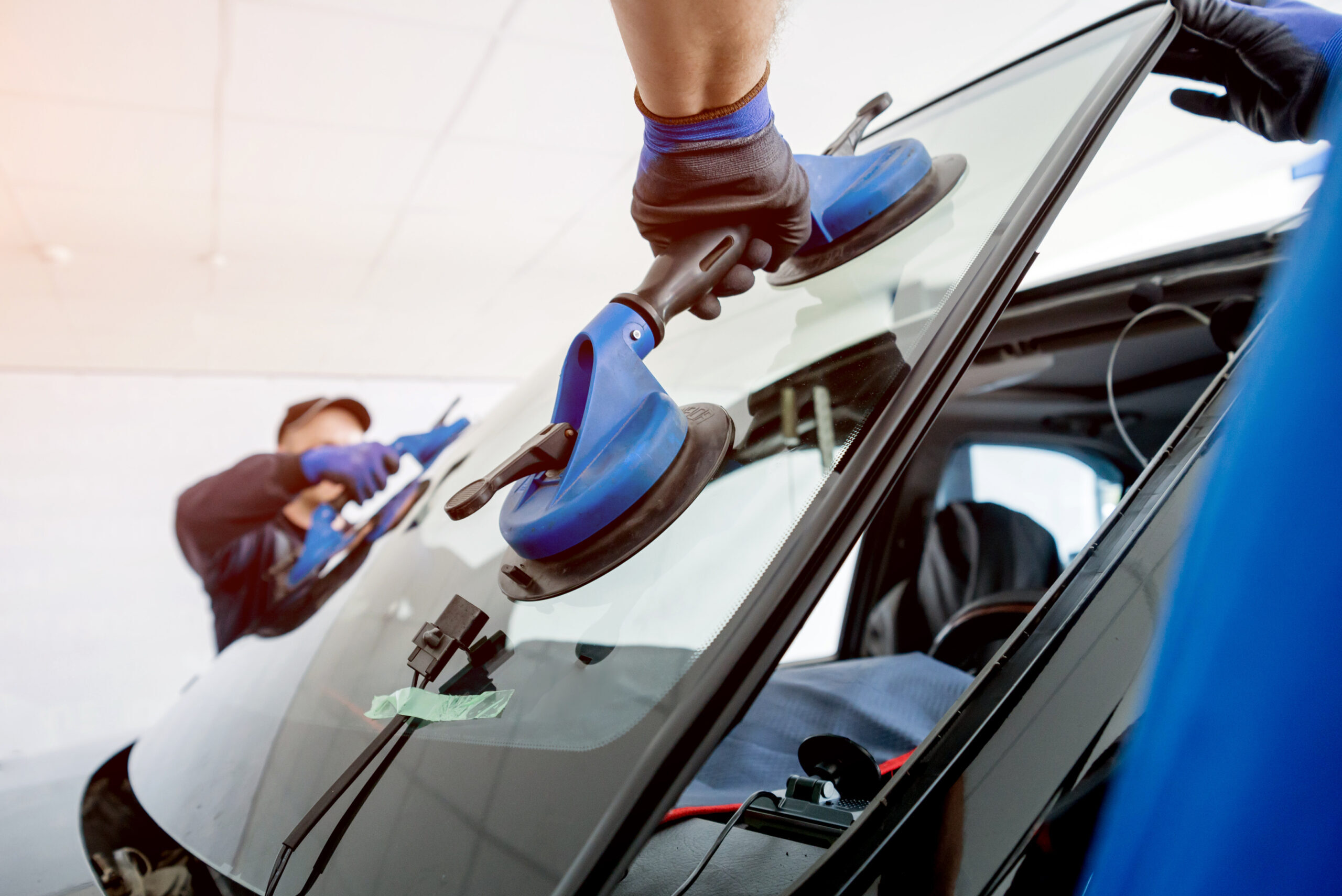 Automobile special workers replacing windscreen or windshield of a car in auto service station garage 