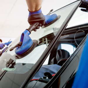 Automobile special workers replacing windscreen or windshield of a car in auto service station garage. Automobile special workers replacing windscreen or windshield of a car in auto service station garage